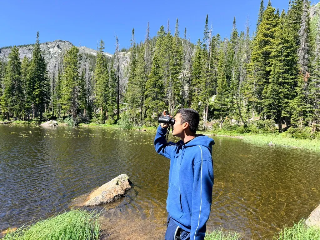 Aditya looking through binoculars across a mountain lake