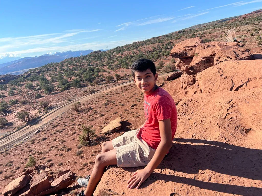 Aditya sitting on red sandstone above a desert valley