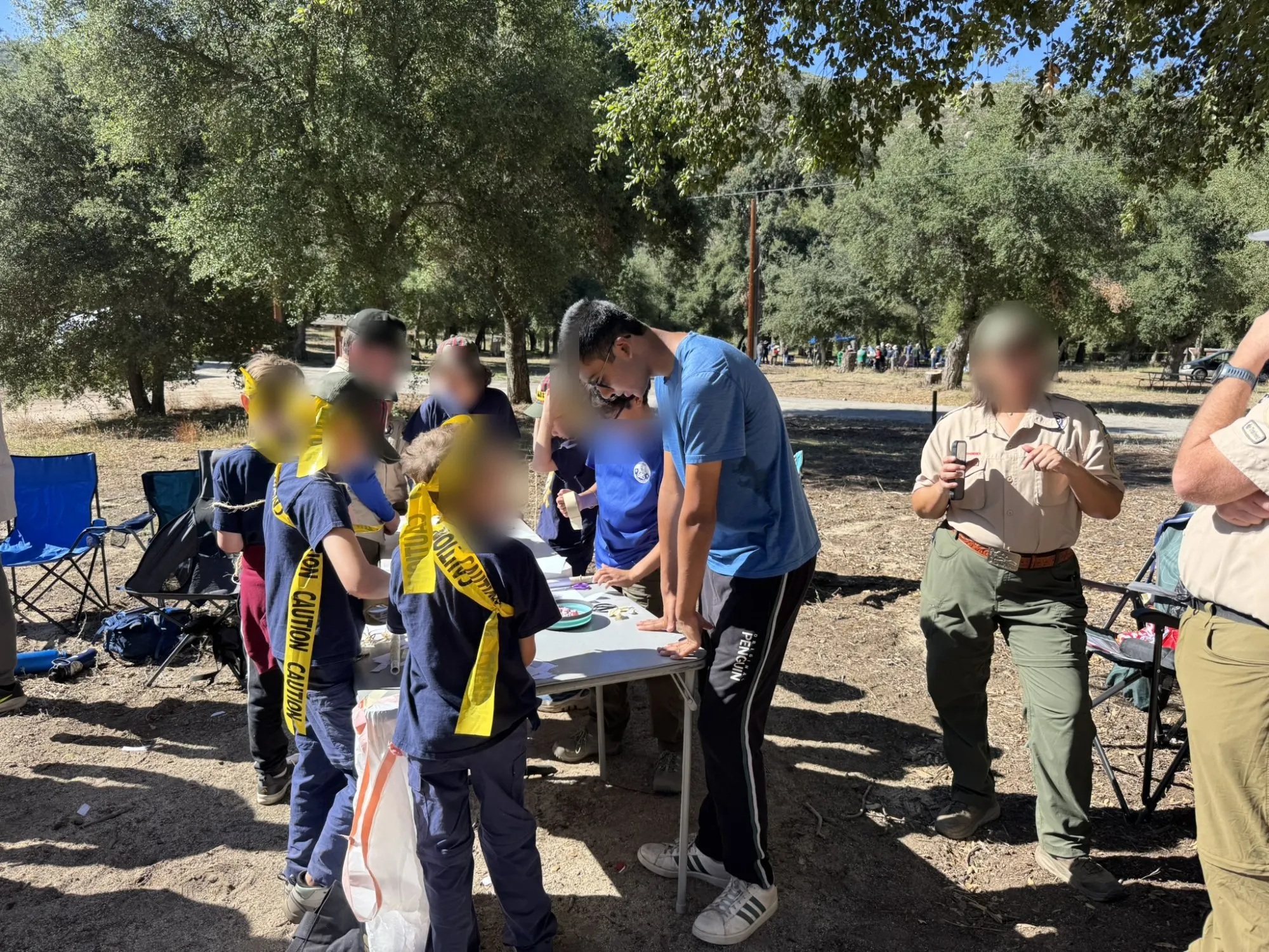Aditya in a blue shirt helping younger scouts at an outdoor table; other faces blurred